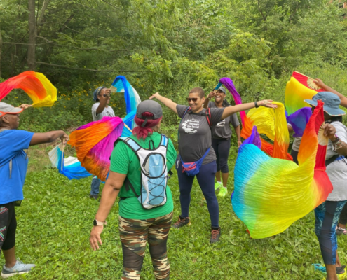 Women gathered in a circle waving rainbow colored fabric