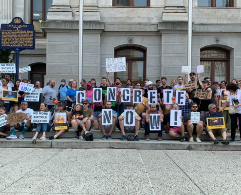 Group of people outside Philadelphia's City Hall holding signs that read "Concrete Now" at a rally for safer bike lanes.