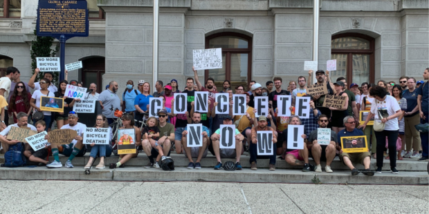 Group of people outside Philadelphia's City Hall holding signs that read "Concrete Now" at a rally for safer bike lanes.