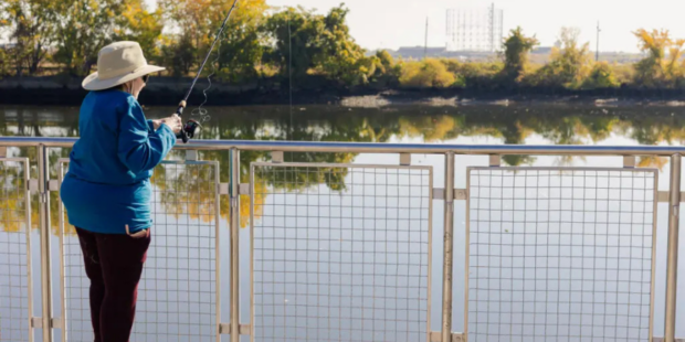 woman in a blue shirt and tan hat fishing off a pier