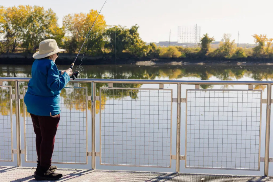 woman in a blue shirt and tan hat fishing off a pier