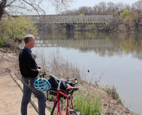 Man standing on landing next to a bike with a blue helmet looking into the river