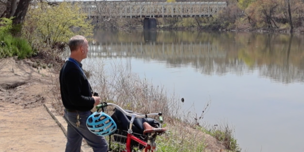 Man standing on landing next to a bike with a blue helmet looking into the river