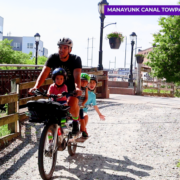 Man riding a cargo bike with three children. One child is on a saddle in the front and two are in a cargo seat in the back.