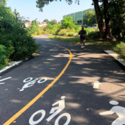one person walking on a paved trail that has a yellow line splitting the middle of the trail with pedestrian and cyclist icons on the trail ground