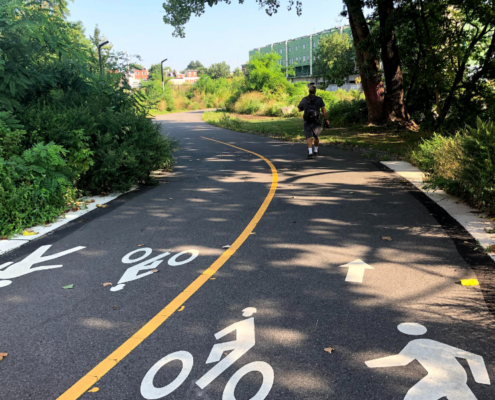one person walking on a paved trail that has a yellow line splitting the middle of the trail with pedestrian and cyclist icons on the trail ground
