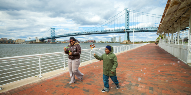 two people in winter jackets blowing bubbles while walking along the Ulysses Wiggins Waterfront Promenade