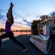 a woman standing in a yoga pose on a boat launch during the sunset