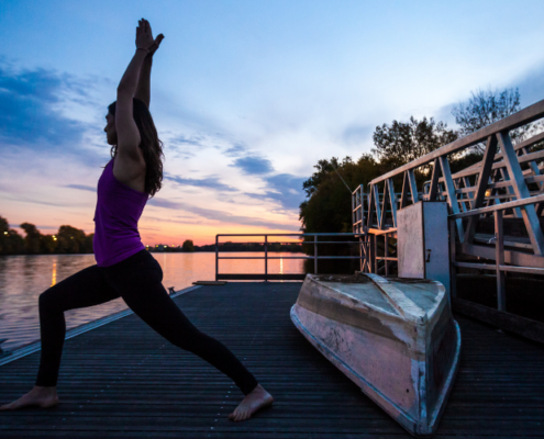a woman standing in a yoga pose on a boat launch during the sunset