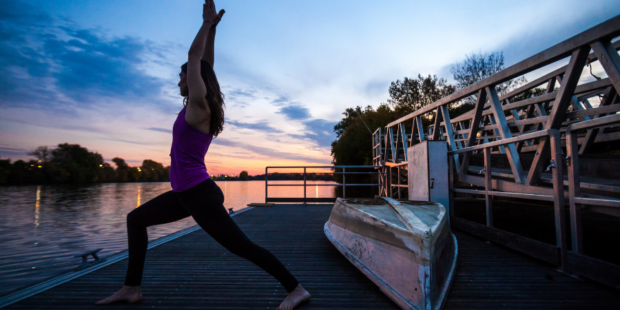 a woman standing in a yoga pose on a boat launch during the sunset