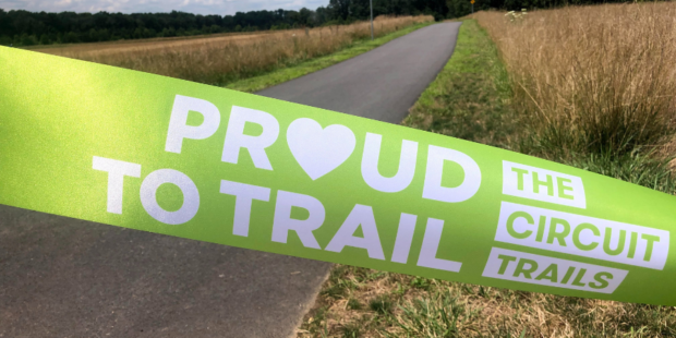 Green proud to trail ribbon across a newly paved trail before a ribbon cutting ceremony