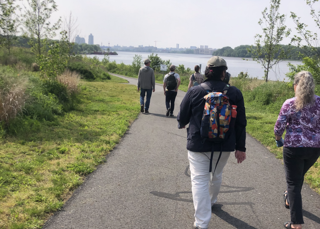 group of people facing away from the camera walking on a trail in Cramer Hill Waterfront Park on a nice spring day