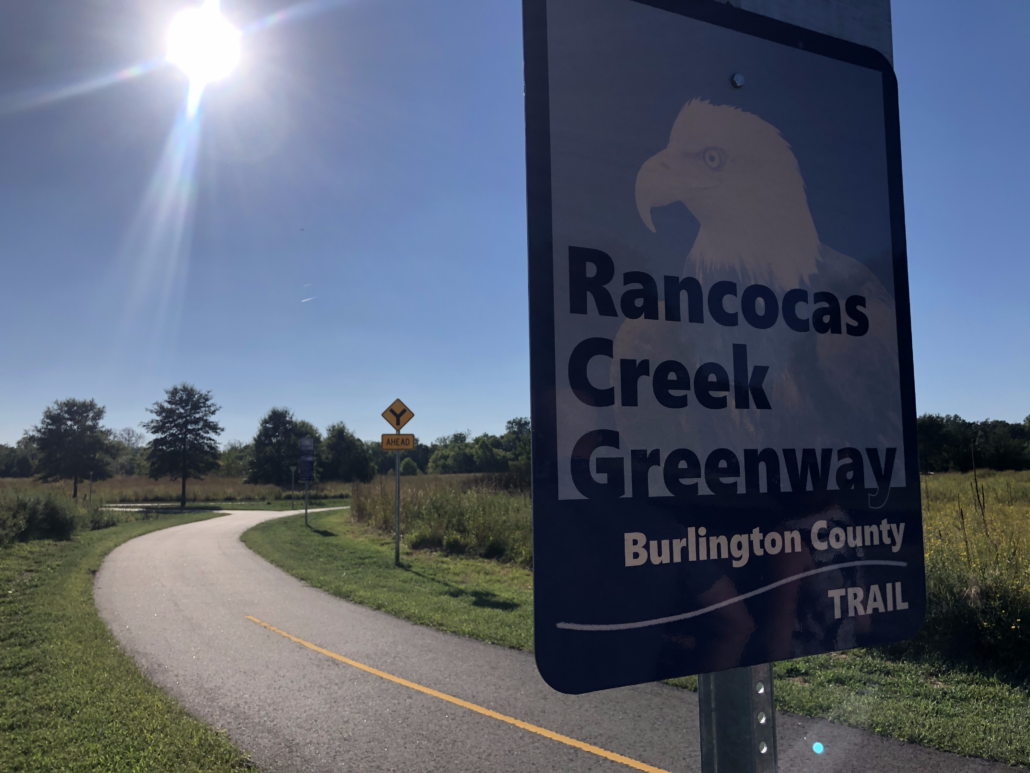 close up of Rancocas Creek Greenway sign along the trail with the paved trail in the background