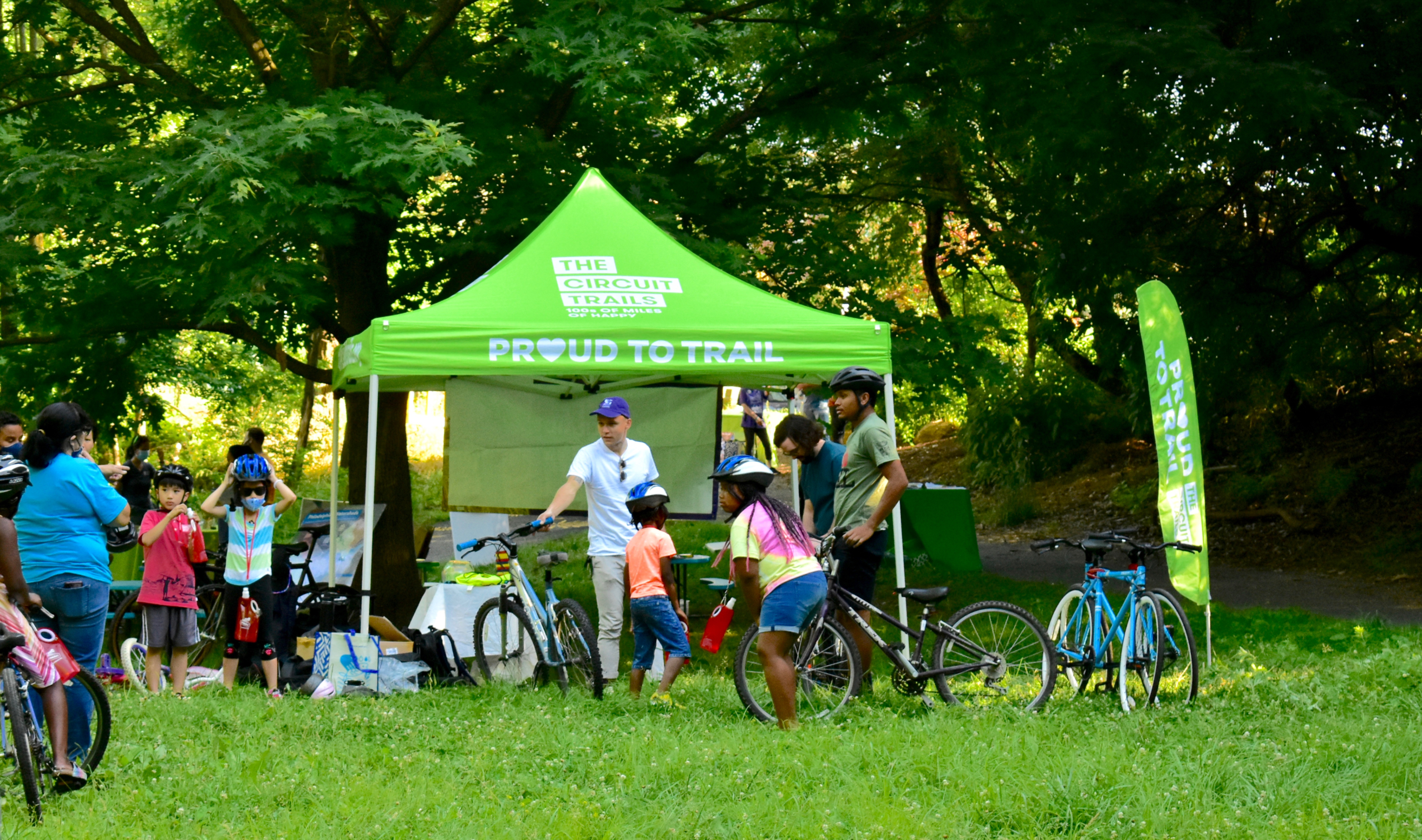 a group of children with bikes gather around a green Circuit Trails pop up tent in Tacony Creek Park