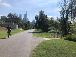 Man running on trail with city skyline in background.